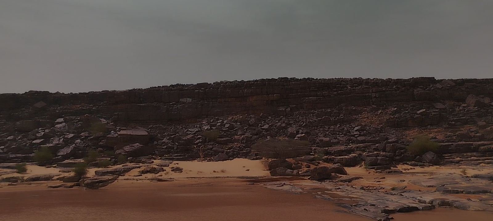 Rocky Adrar plateau and desert sand under a stormy sky