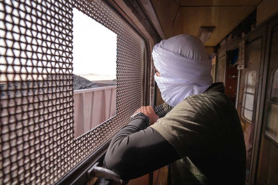 A traveler in a turban looking out of the iron ore train window across the Mauritanian Sahara